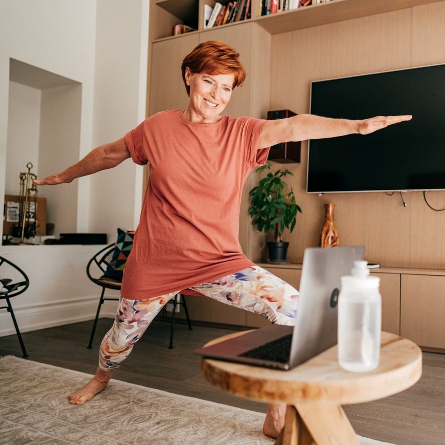 Woman in her 60s with glasses exercising on the floor at home, engaged and smiling