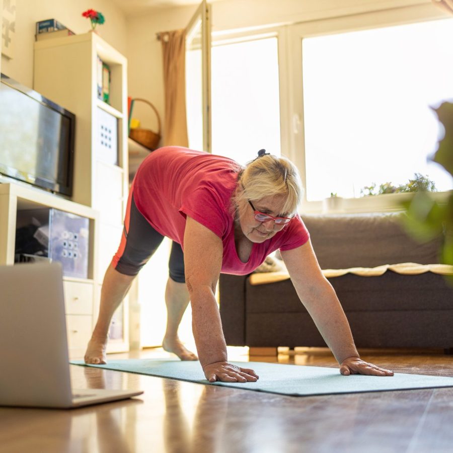 Woman in a deep stretch on a yoga mat, focused on her laptop screen during a session