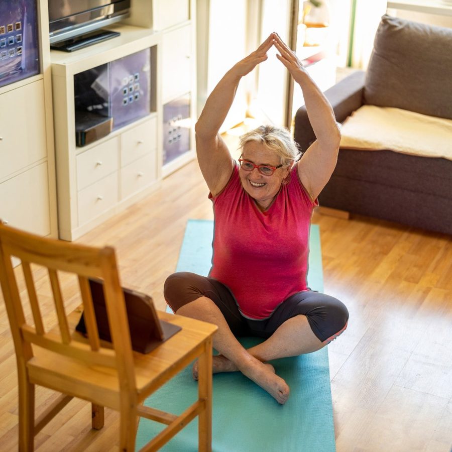 Woman smiling and relaxed during a virtual stretching session, tablet visible nearby
